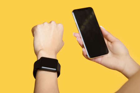Devices for sport. Young woman with smart watch and smartphone with blank black screen, yellow backgroundの写真素材