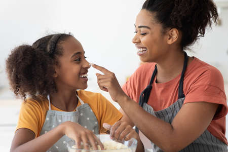 Closeup of black woman staining her daughter nose with flour