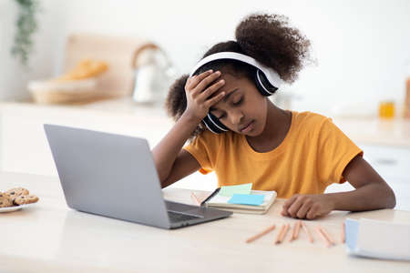 Upset black school girl doing homework, kitchen interior