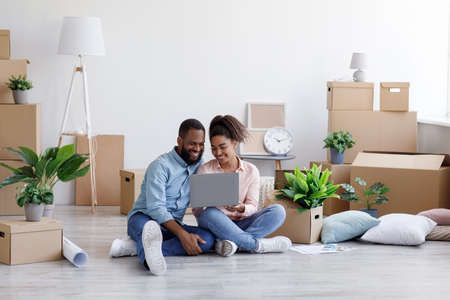 Glad young african american family resting, sitting on floor among cardboard boxes with things