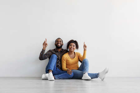 Smiling african american family sit on floor over gray wall background, showing fingers up at copy spaceの写真素材