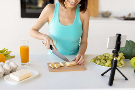 Young blogger preparing fruit salad, cutting banana and recording new video recipe for her food blogの写真素材