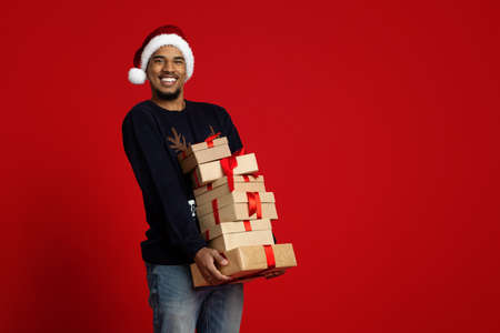 Cheerful african american man in santa hat holding christmas giftsの写真素材