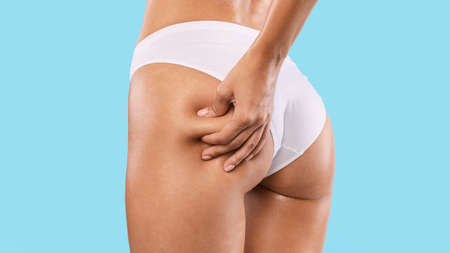 Unrecognizable young woman pinching her buttocks, examining cellulite