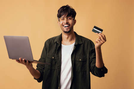Emotional indian guy with new modern laptop and credit cardの写真素材
