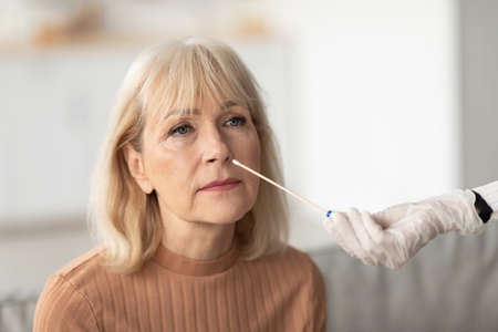 Unrecognizable Nurse Making Covid-19 PCR Test For Senior Woman Indoorsの写真素材