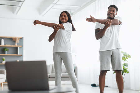 Young black couple doing arm stretch exercise watching online tutorialの写真素材