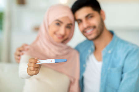 Closeup of positive pregnancy test in muslim woman hands cuddling with her husband and smiling to cameraの写真素材