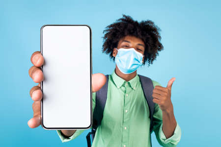 Black guy in protective face mask showing cellphone, mockupの写真素材