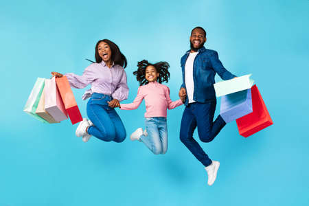 Excited cheerful black people jumping and holding shopping bagsの写真素材