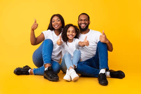 Excited African American people gesturing thumbs up sitting on floorの写真素材
