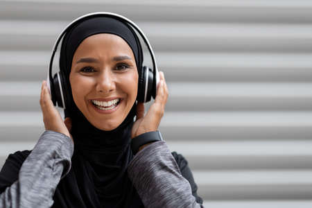 Cheerful Muslim Woman In Hijab And Wireless Headphones Listening Music Outdoorsの写真素材