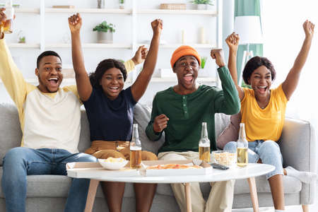 Joyful black hipsters football fans watching game on TVの写真素材