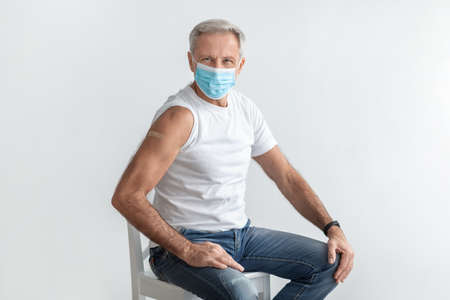 Senior Man Wearing Mask Showing Vaccinated Arm Sitting In Studioの写真素材