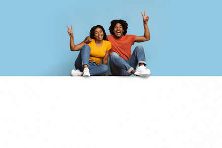 Carefree black couple sitting on blank board, gesturingの写真素材