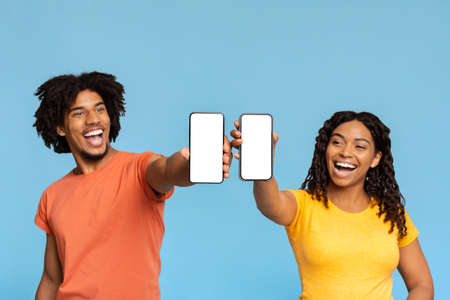 Jolly black man and woman showing smartphones with blank screensの写真素材