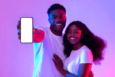 African American couple showing smartphone with mockup, advertising new application or website in neon lightの写真素材