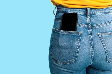 Cropped view of female having cellphone with blank screen in jeans pocket on blue studio background, mockupの写真素材
