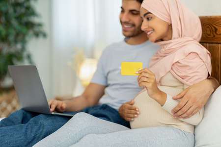 Muslim mother and father shopping online for their future baby, using laptop computer and credit cardの写真素材