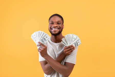 Im rich. Overjoyed african american man showing money cash and smiling to camera, posing over yellow backgroundの写真素材