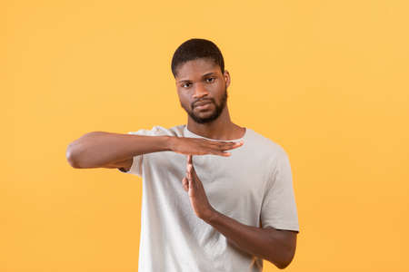 African american guy showing TIME OUT or STOP gesture taking break or pause, yellow studio background,の写真素材