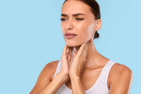 Young woman suffering from sore throat, blue studio
