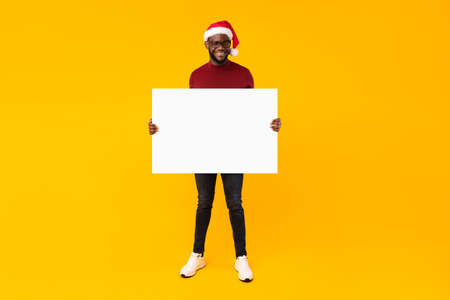 Black Guy Showing Blank Poster For Christmas Advertisement, Yellow Backgroundの写真素材