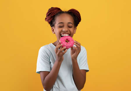 Sweet tooth black girl eating donut on yellowの写真素材