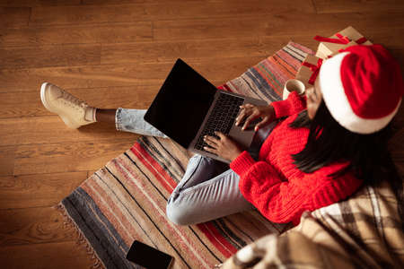 Top view of young black lady using laptop with empty screen at home, shopping for Christmas gifts online, mockupの写真素材