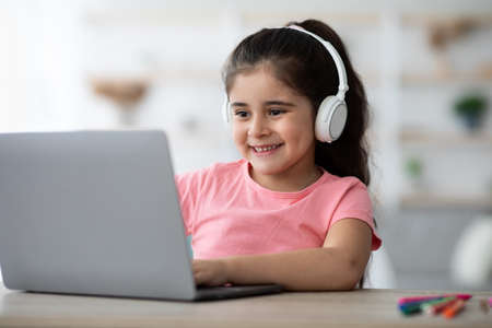Cute Little Arab Girl In Wireless Headphones Having Online Lesson On Laptop