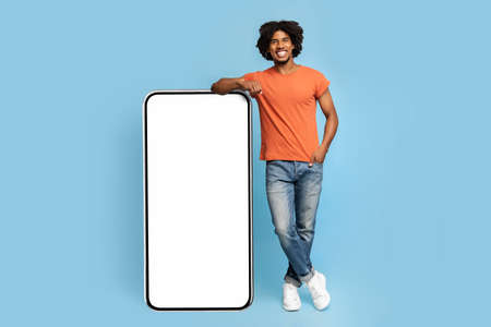 Happy black guy standing by big cellphone, mockup
