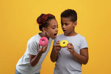 Sweet tooth black girl biting her brothers donutの写真素材