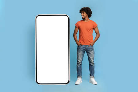 Stylish black guy looking at big smartphone with empty screen