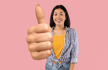 Stylish asian woman showing thumb up on pink