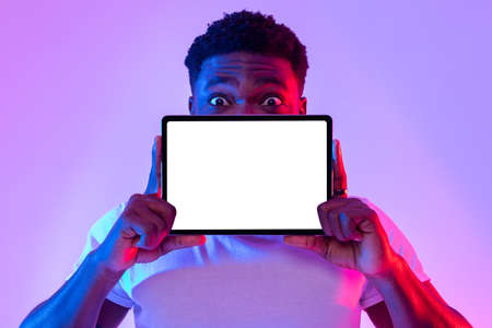 Tablet screen mockup. Cool black man covering face with blank touch pad, recommending new app or website in neon lightの写真素材