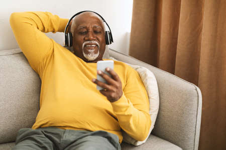 Senior African American Man Listening Music On Smartphone At Homeの写真素材