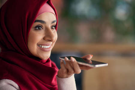 Closeup of pretty muslim woman recording audio message on cellphoneの写真素材