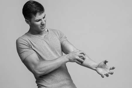 Despaired millennial caucasian male suffering from irritation and scratching skin on hand with painful facial expressionの写真素材