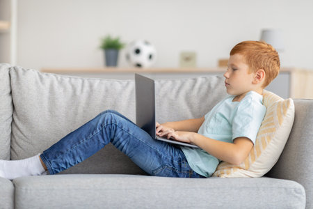 Redhead boy using laptop, playing online video game, side viewの写真素材