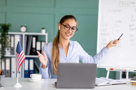 Happy young teacher conducting English lesson on web, using laptop, explaining grammar rules from...