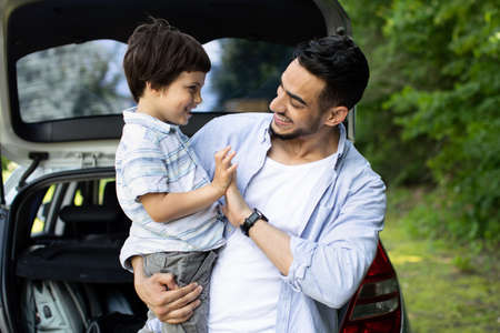 Happy Arab Man With Little Son Standing Near Car With Open Trunk