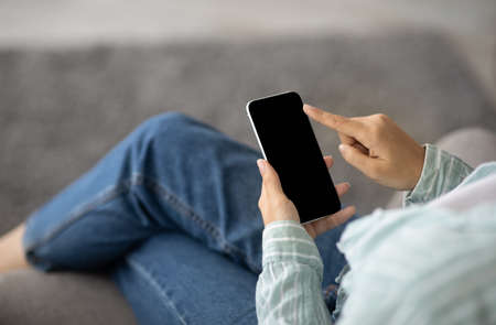 Young Indian woman using smartphone with empty screen at home, mockup for mobile app or website...
