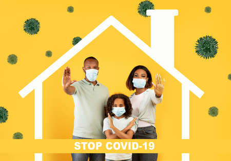 Social distancing and Covid-19 pandemic. African american family in medical masks showing STOP gesture yellow backgroundの写真素材