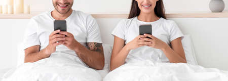 Cropped smiling caucasian young man and woman typing on smartphones, chatting online and surfing in internetの写真素材