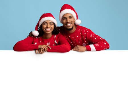 Cheerful black lovers leaning on empty horizontal advertising board
