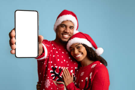 Loving black couple celebrating xmas together, showing cellphone, mockup