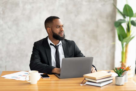 African American man using laptop thinking looking away