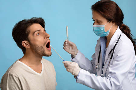 Female Nurse Holding Swab Making Oral PCR Coronavirus Test For Young Man