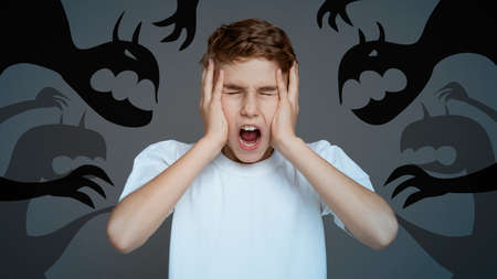 Scared little boy closing eyes, covering ears and screaming in panic, fighting fantasy monsters and inner fears, collageの写真素材