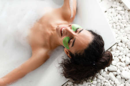 Sensual young lady lying in bubble bath with eye patches, top viewの写真素材
